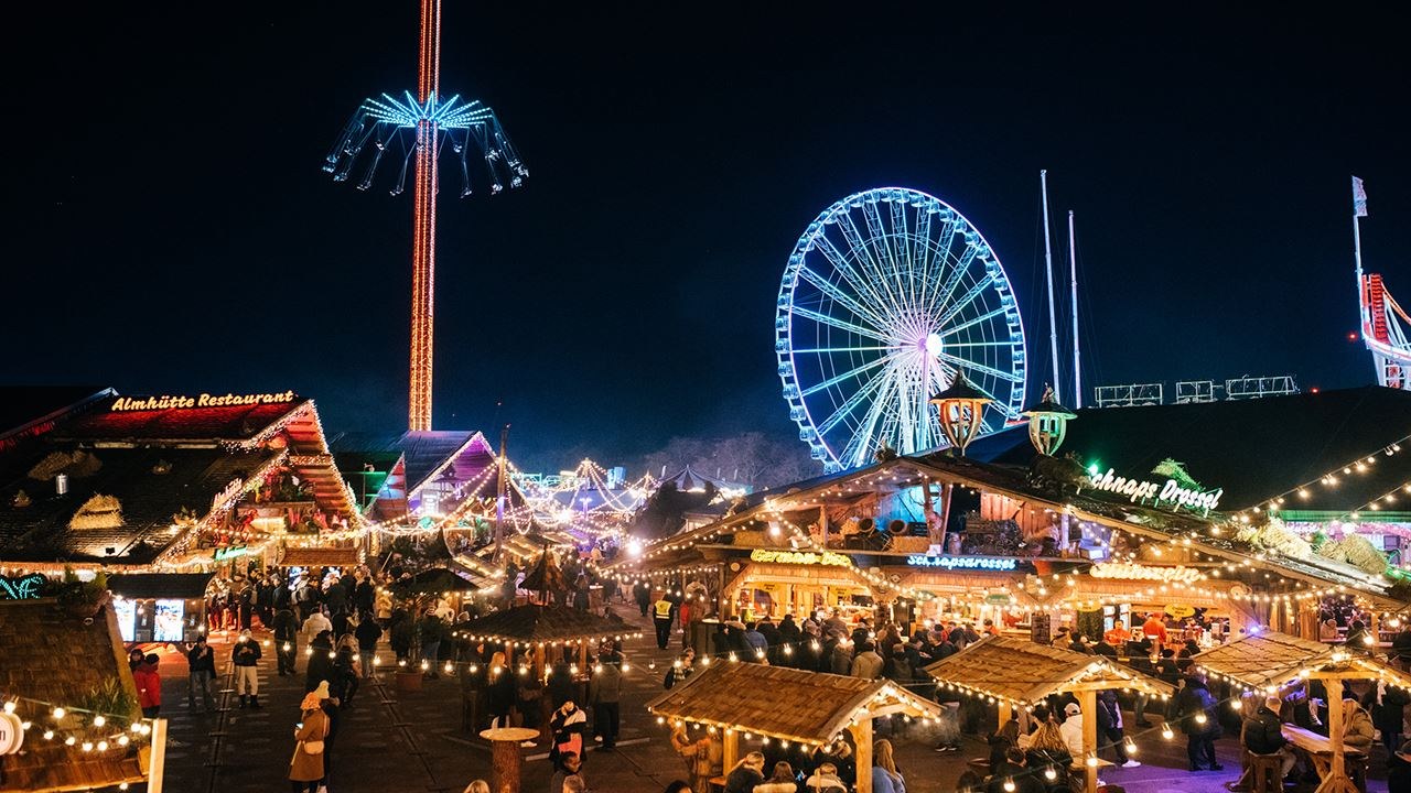 Illuminated rides, a Ferris wheel and wooden Christmas chalets at Winter Wonderland after dark
